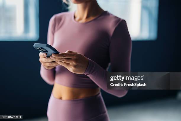 woman using smartphone in lavender activewear during a fitness break - athleisure stock pictures, royalty-free photos & images