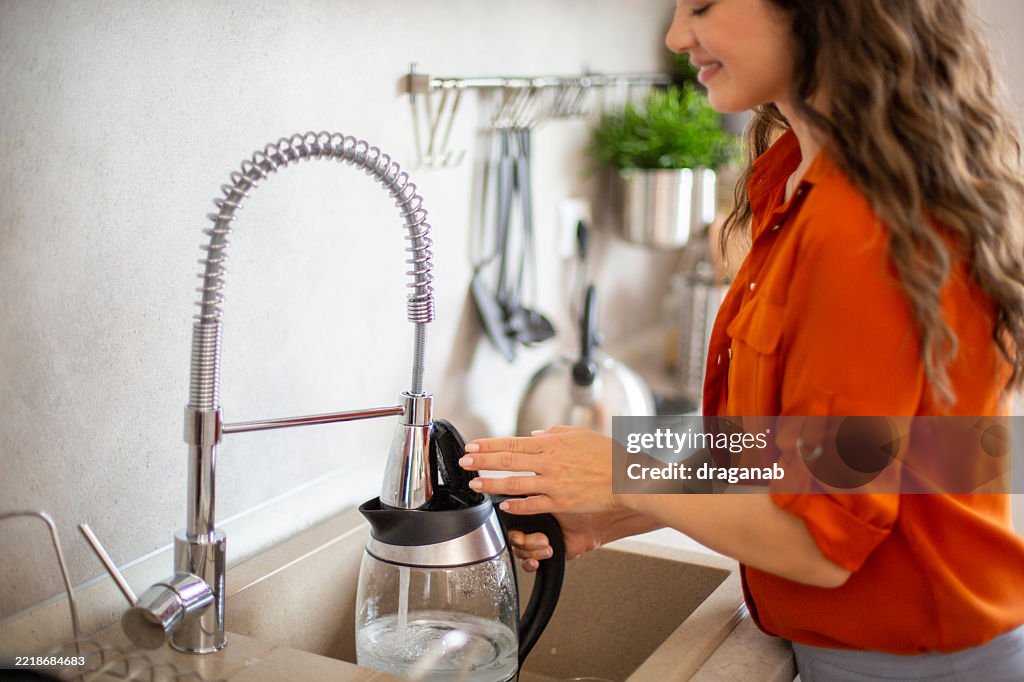 Frau füllt Wasserkocher mit Leitungswasser in moderner Küche
