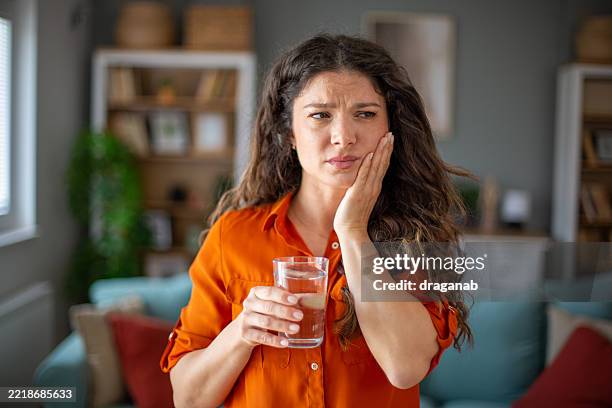 woman suffering from strong tooth pain holding glass of water at home - human teeth stock pictures, royalty-free photos & images