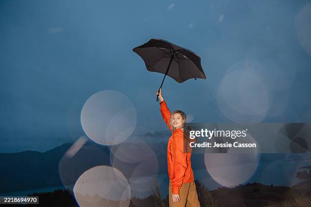 a woman stands with an umbrella in moody landscape - una mujer de mediana edad solamente fotografías e imágenes de stock