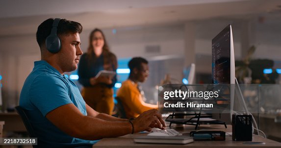 Focused Developer Working on Code at Modern Office While Colleagues Collaborate in Background Focused Developer Working on Code at Modern Office While Colleagues Collaborate in Background