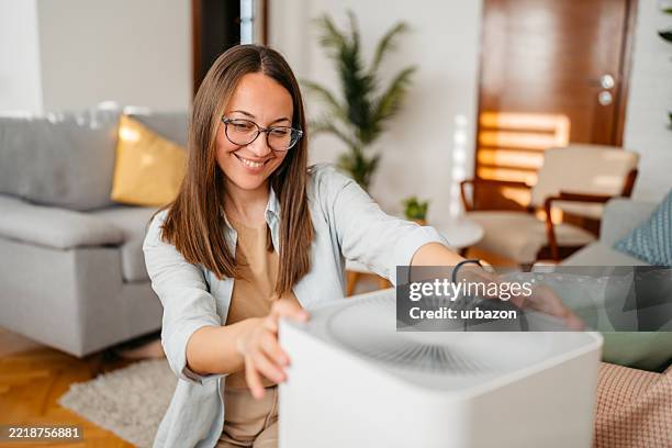 young woman turing on the air purifier at home - air purifier stock pictures, royalty-free photos & images