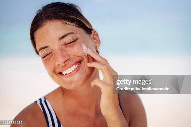 mujer aplicando protector solar en una playa soleada - vestido crema fotografías e imágenes de stock