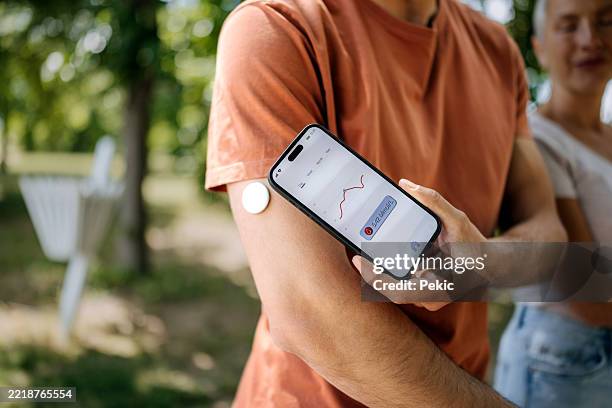 man checking blood sugar level on phone while standing with partner in park - glucose stockfoto's en -beelden