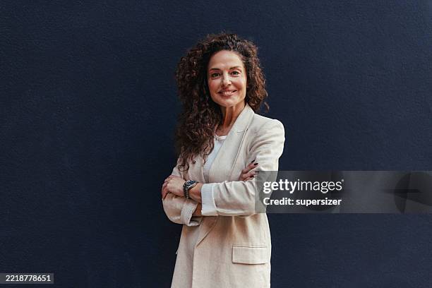 mujer sonriente con atuendo beige con los brazos cruzados - una mujer de mediana edad solamente fotografías e imágenes de stock