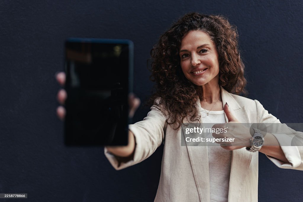 Smiling Woman Holding Tablet Against a Dark Wall