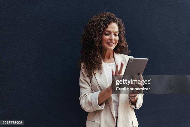 mujer segura de sí misma usando la tableta contra el fondo oscuro - una mujer de mediana edad solamente fotografías e imágenes de stock