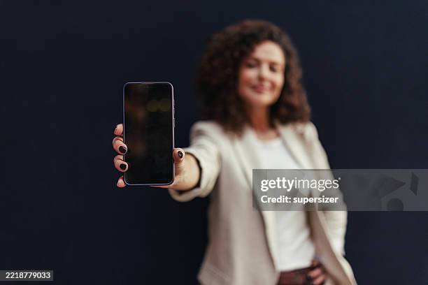 mujer segura de sí misma que muestra el teléfono inteligente en un entorno profesional - una mujer de mediana edad solamente fotografías e imágenes de stock