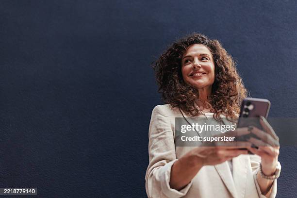 mujer alegre sosteniendo el teléfono con una sonrisa - una mujer de mediana edad solamente fotografías e imágenes de stock
