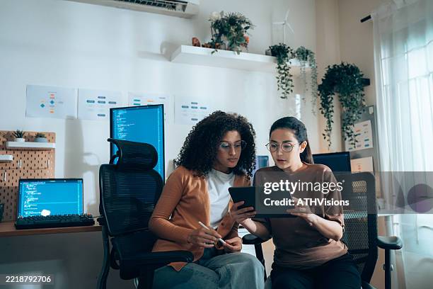 women in tech collaborate on ui review with tablet and coding monitors in background - sob proteção imagens e fotografias de stock