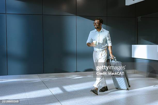 viajero de negocios con maleta caminando por la terminal del aeropuerto brillantemente iluminada - pasajero fotografías e imágenes de stock