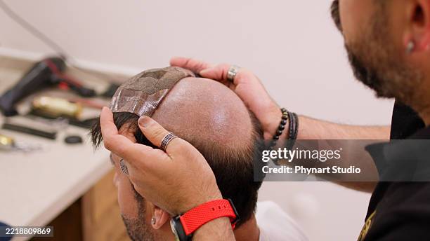 hairstylist attaching a wig to a man using adhesive stripes, barber applying and styling a hair system for male client - wig stock pictures, royalty-free photos & images