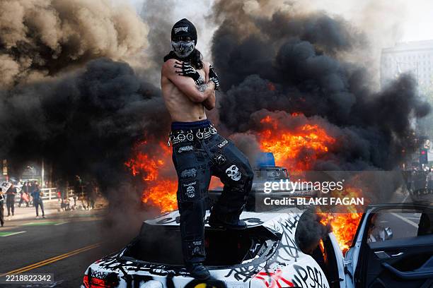 This picture taken on June 8, 2025 shows a protestor standing on top of a burning Waymo vehicle during a demonstration following federal immigration...