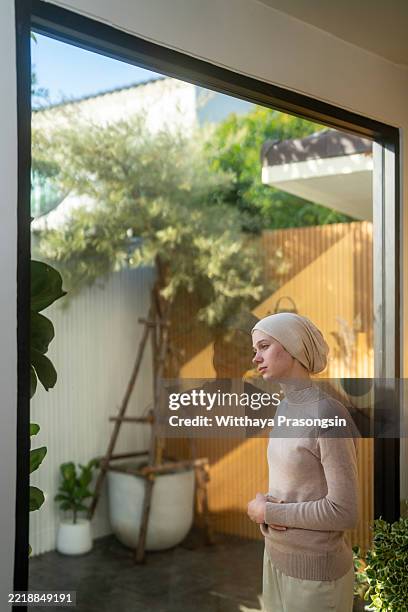 young cancer patient feeling sick and looking out the window - laubsäge stock-fotos und bilder