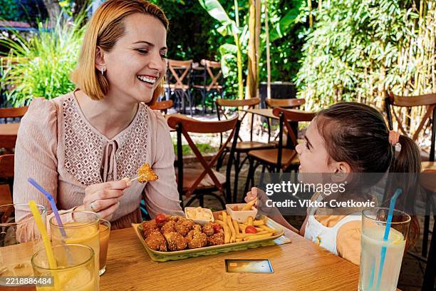 mother and daughter enjoying a meal together at a restaurant - eating chicken nuggets stock pictures, royalty-free photos & images