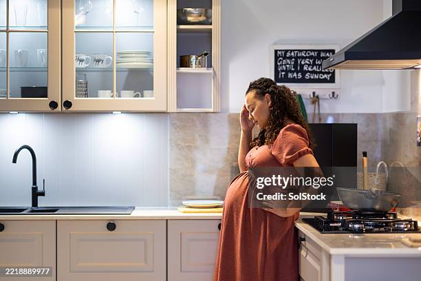 sad pregnant woman standing alone in kitchen - hand on hip stock pictures, royalty-free photos & images