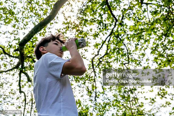 a boy in white t-shirt drinking from the metal water bottle - green t shirt stock pictures, royalty-free photos & images