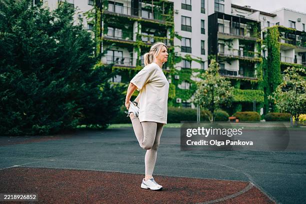 smiling mature woman stretching her leg in residential neighborhood - quadriceps muscle stock pictures, royalty-free photos & images