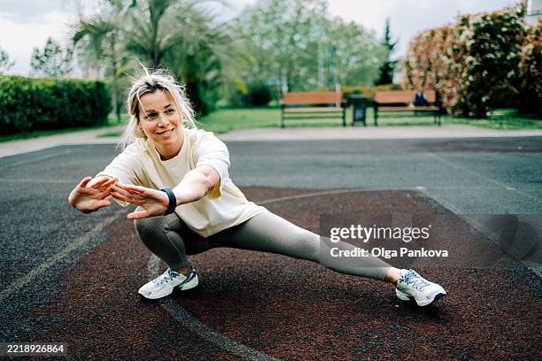 smiling mature woman stretching her leg in residential neighborhood - heup stockfoto's en -beelden