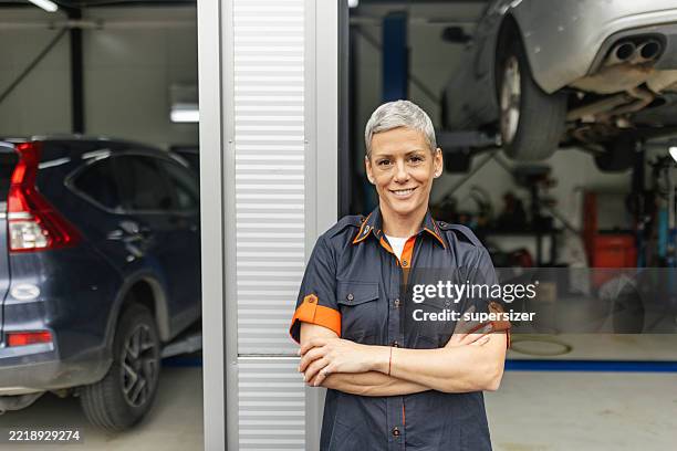 mecánico sonriente posa con confianza en el garaje - una mujer de mediana edad solamente fotografías e imágenes de stock