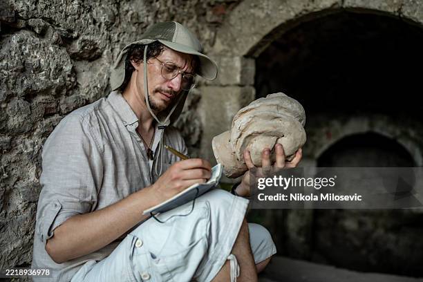 archäologe, der ein antikes artefakt an einer historischen stätte untersucht - archäologe stock-fotos und bilder