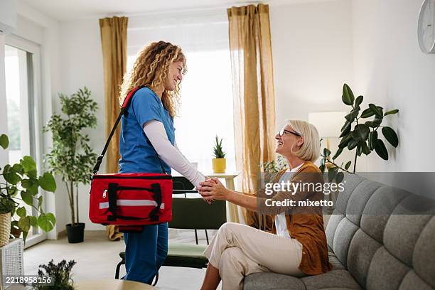 enfermera sonriente que estrecha la mano de una mujer mayor - visita a domicilio fotografías e imágenes de stock