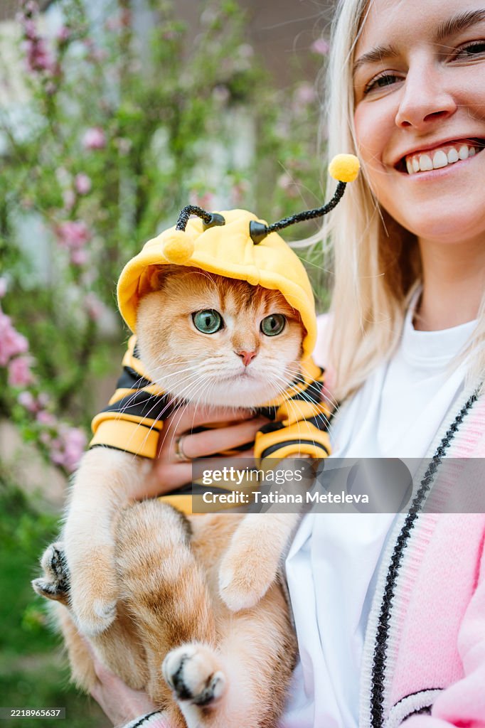 Woman walking with ginger cat in bee costume in park