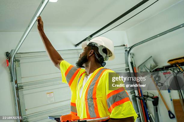 young adult african american male electrician inspecting garage door opener during daytime indoors - installing ceiling light fixture stock pictures, royalty-free photos & images