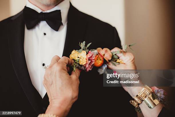 mother of groom pinning on flower boutonniere for wedding ceremony - tuxedo stock pictures, royalty-free photos & images