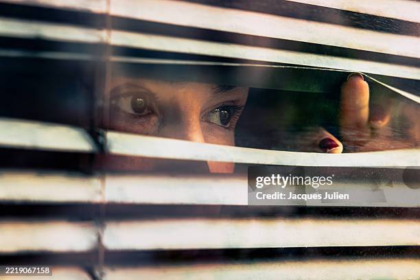 woman peering through window blinds - spion stockfoto's en -beelden