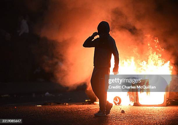 Rioter walks past flames as PSNI officers in riot gear respond to a third night of civil unrest on June 11, 2025 in Ballymena, Northern Ireland....
