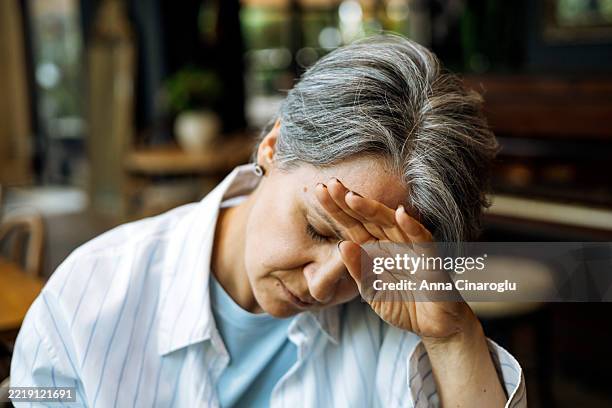an older woman with gray hair, covering her face with her hand, seems to be experiencing a moment of stress. - frowning stock pictures, royalty-free photos & images