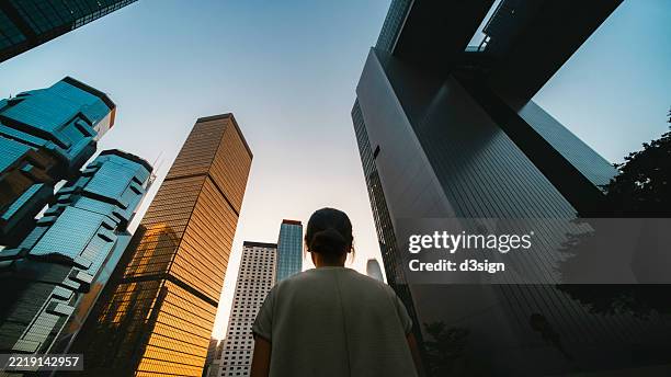 low angle, ultra-wide shot of determined young asian businesswoman looking ahead while standing against contemporary corporate skyscrapers in financial district. woman in business. striving for success. female equality and empowerment - ultra rich people stock pictures, royalty-free photos & images