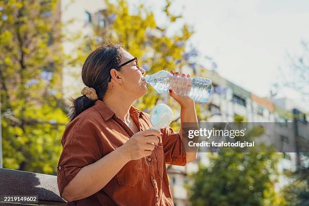 femme buvant de l’eau et utilisant un ventilateur électrique portable. souffrir d’un coup de chaleur - éventail photos et images de collection