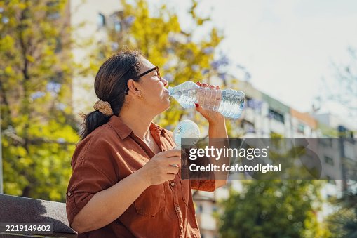 Woman drinking water and using portable electric hand fan. Suffering from heat stroke Woman drinking water and using portable electric hand fan. Suffering from heat stroke