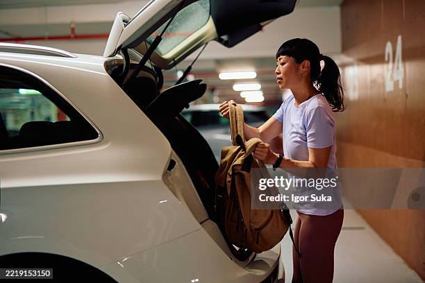 woman putting backpack in car trunk at parking garage - convenience stock pictures, royalty-free photos & images