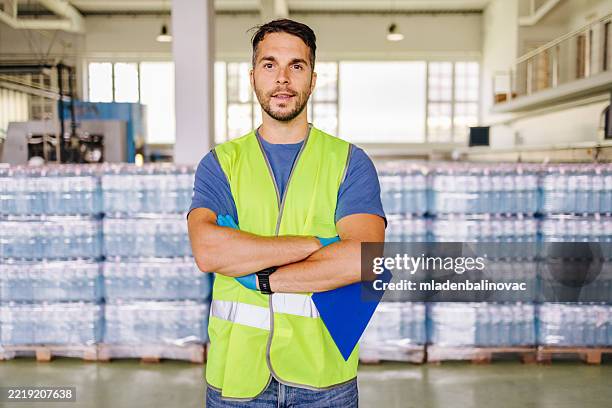 supervisor sonriendo con los brazos cruzados en el almacén de la planta embotelladora - material reflector de seguridad fotografías e imágenes de stock