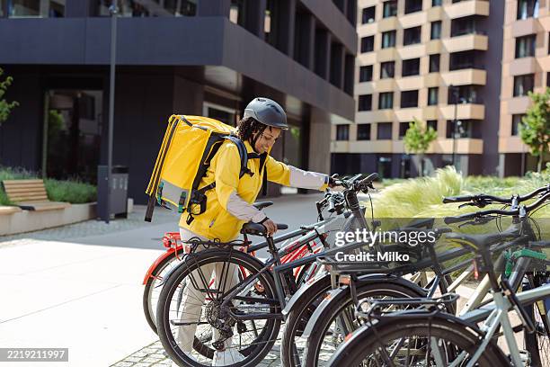 weibliche kurierin sichert das fahrrad und bereitet sich auf die umweltfreundliche paketzustellung in der stadt vor - fahrradkurier stock-fotos und bilder