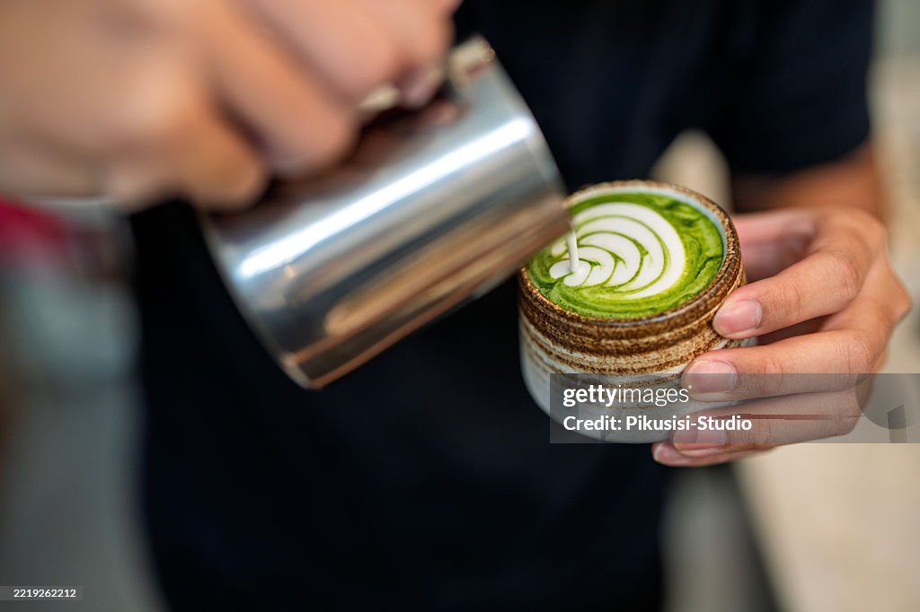 Barista versant du lait dans un matcha latte avec Latte Art