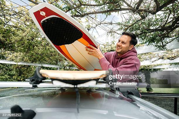 man loading surfboard onto vehicle roof - car roof rack stock pictures, royalty-free photos & images