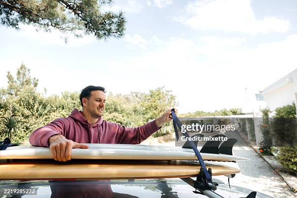 man loading surfboard onto vehicle roof - car roof rack stock pictures, royalty-free photos & images