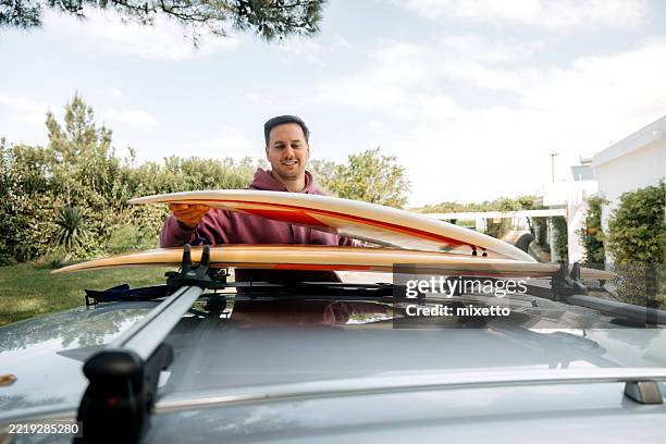 man loading surfboard onto vehicle roof - car roof rack stock pictures, royalty-free photos & images