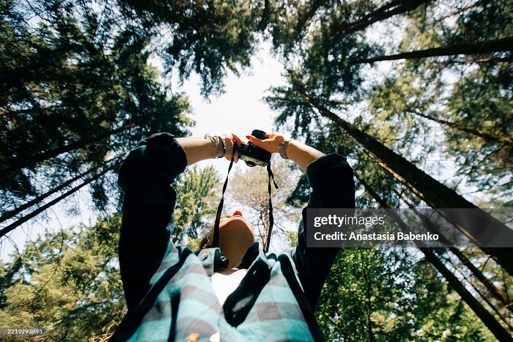 Long angle view of young woman in a green plaid shirt captures the beauty of green forest