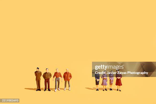 miniature figurines of men and women standing facing each other on yellow background - estereotipo fotografías e imágenes de stock
