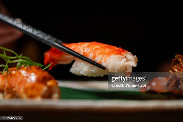stäbchen, die ein stück frisches garnelen-sushi von einem sushi-teller heben. - servierplatte stock-fotos und bilder