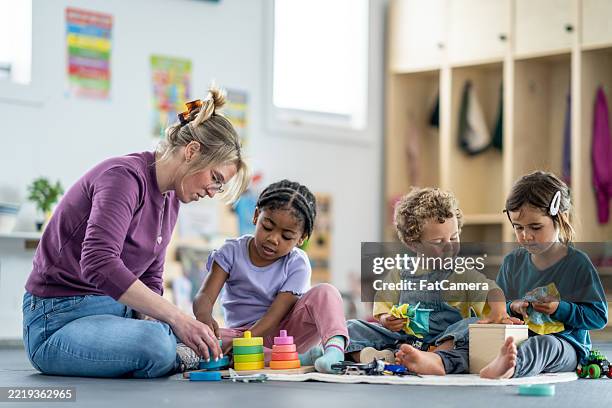 group of young children learning with teacher in colorful daycare classroom - kinderopvang stockfoto's en -beelden