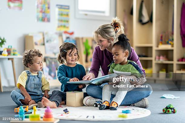 insegnante che legge un libro ai bambini piccoli in un ambiente di sala giochi - bambino di età prescolare foto e immagini stock