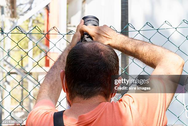 photographer taking pictures behind a wire mesh fence - telelens stockfoto's en -beelden