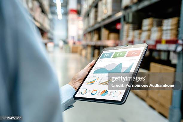 Warehouse employee using digital tablet to monitor business analytics dashboard in modern storage facility for real-time inventory tracking, logistics management, and operational performance.