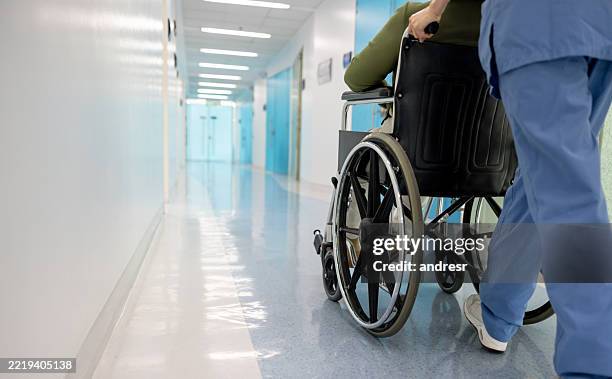 rückansicht einer krankenschwester, die einen patienten im rollstuhl im krankenhaus schiebt - pflege stock-fotos und bilder